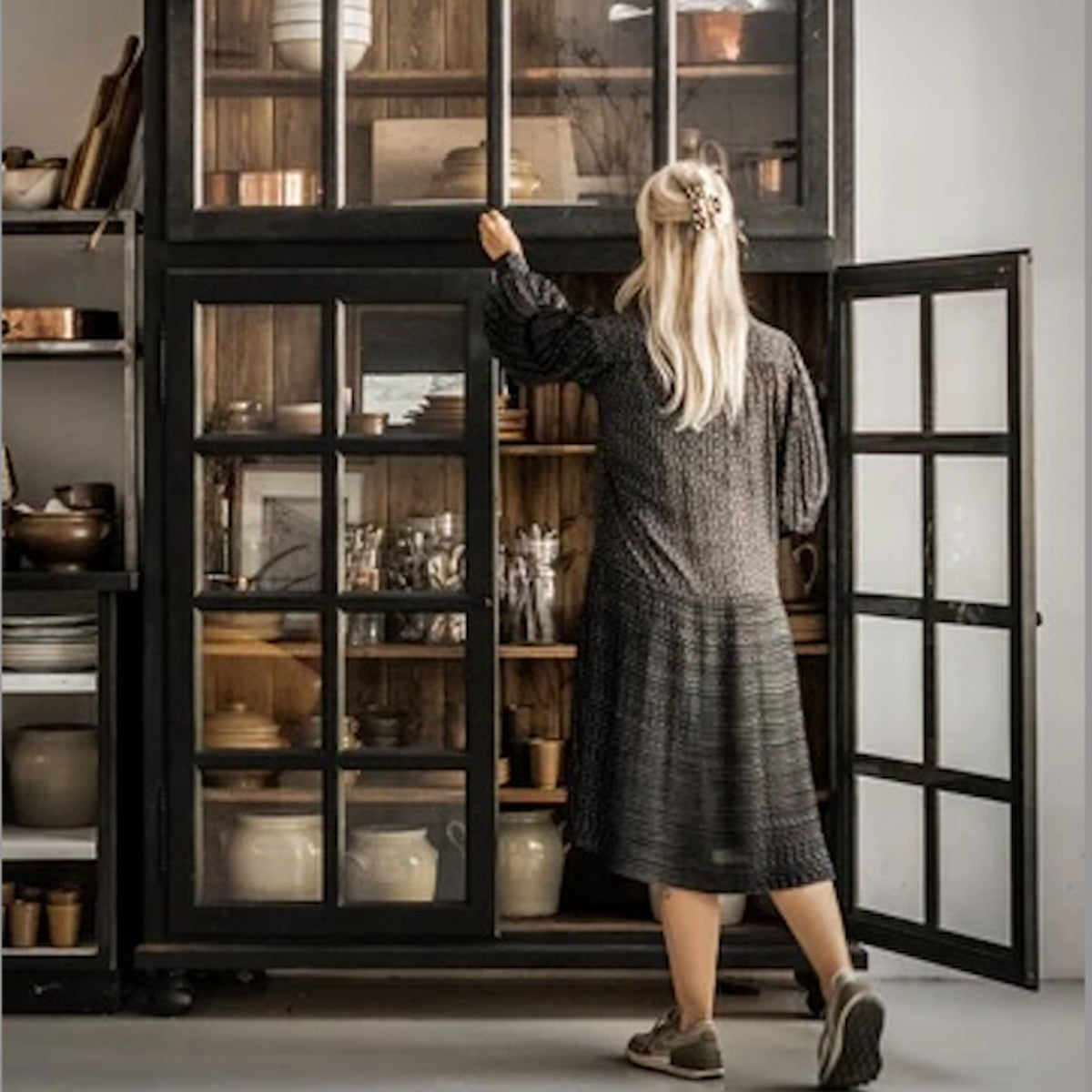 woman in black dress opening large black cabinet
