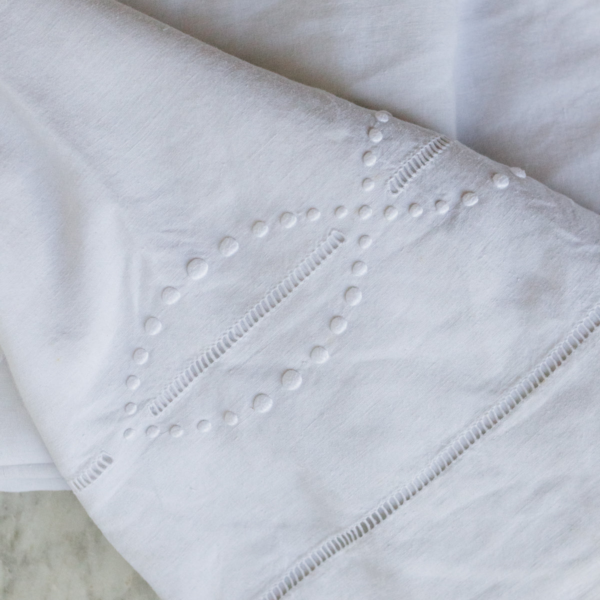Close-up of a white fabric with intricate stitching on a marble surface